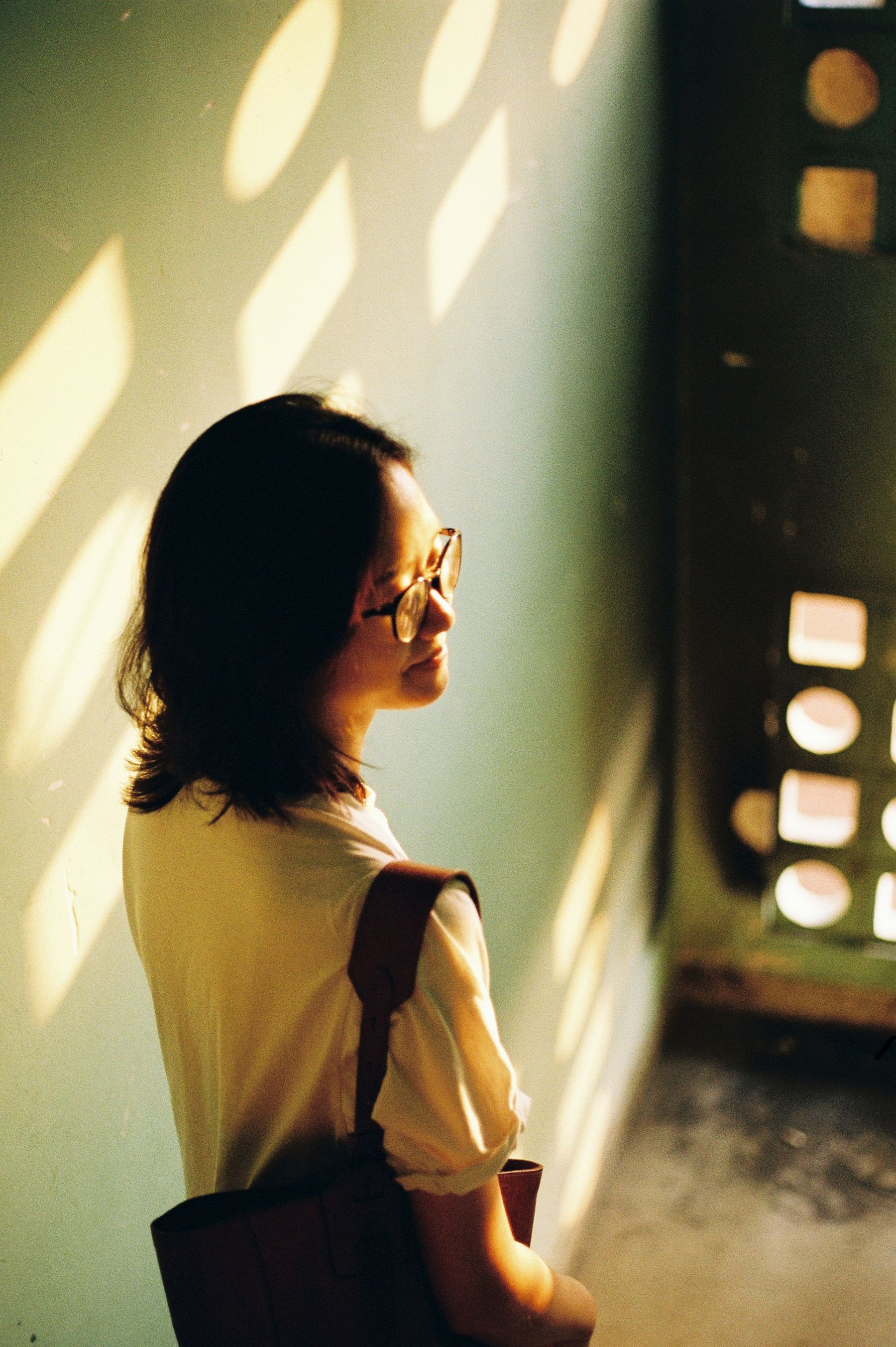 A person standing in warm window light, looking to the side